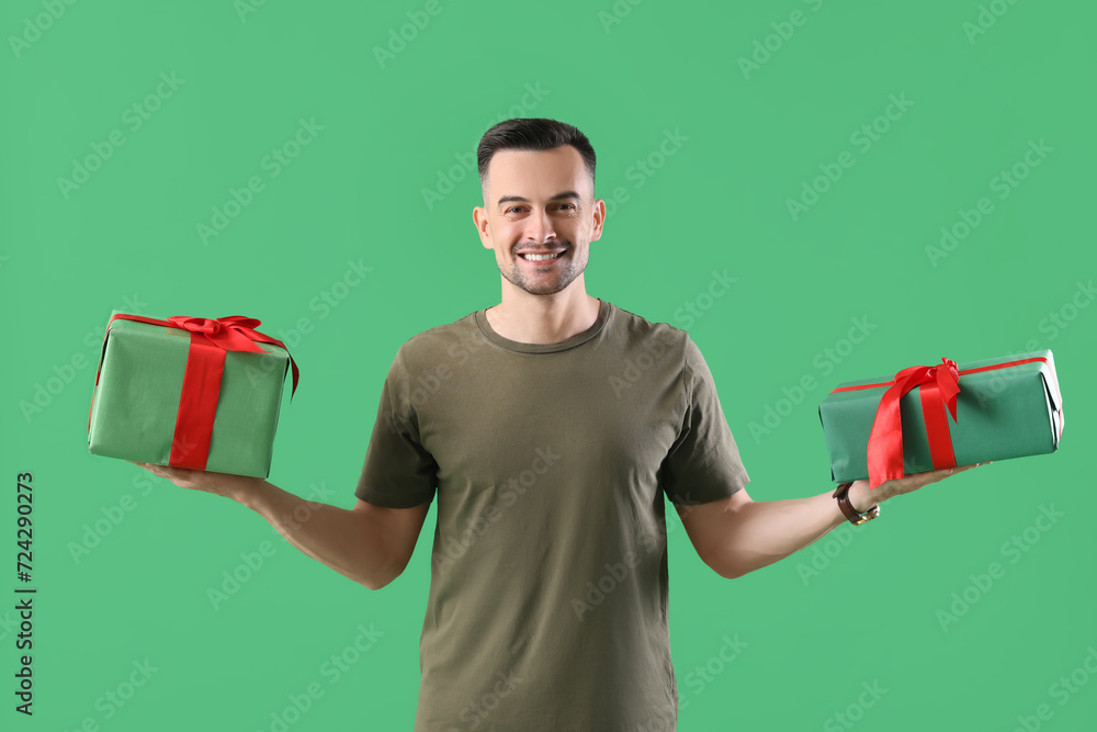 Happy young man with Christmas presents on green background