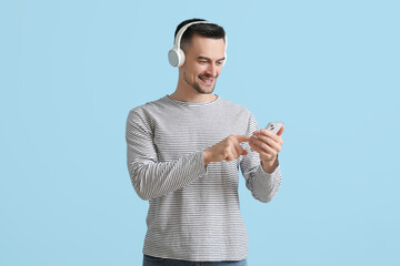 Poster - Happy young man in headphones using mobile phone on blue background