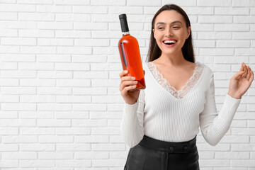 Poster - Beautiful young woman with bottle of wine on white brick background