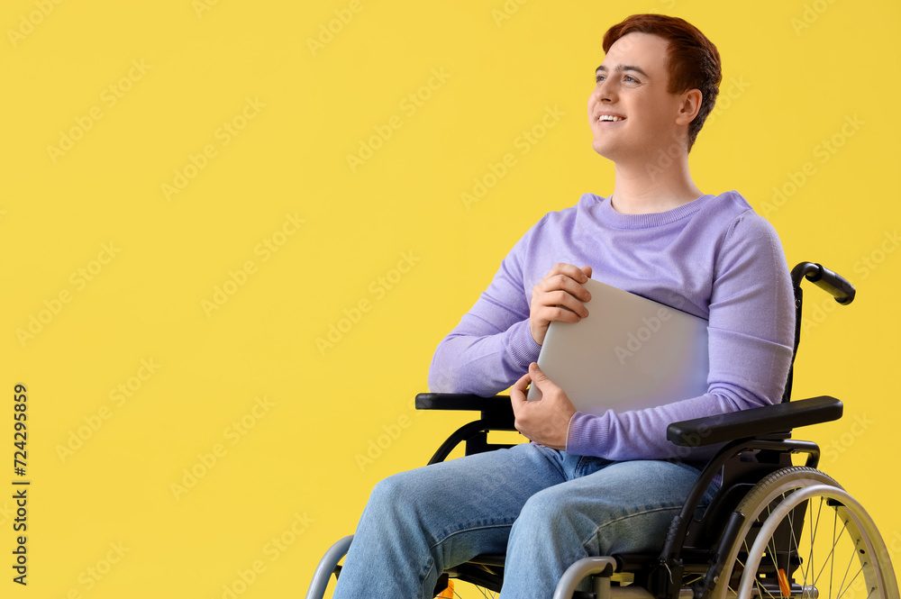 Young man in wheelchair with laptop on yellow background