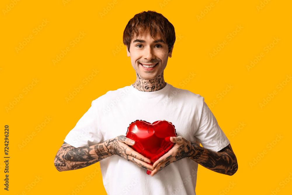 Handsome young man with heart-shaped air balloon on yellow background