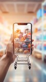 Fototapeta Most - Hand holding smartphone with grocery shopping cart on blurred supermarket background, online shopping concept