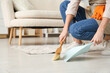 Young woman sweeping floor with dustpan and brush in living room, closeup