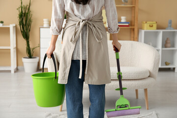 Poster - Young woman with floor mop and bucket in living room, back view