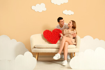 Sticker - Young couple with heart sitting on sofa in clouds near beige wall