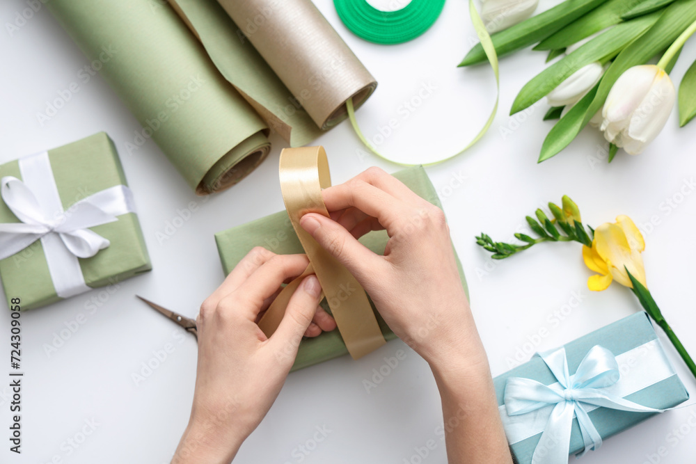 Female hands with gift boxes, wrapping paper and beautiful flowers on white background. International Women's Day