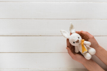 Poster - Hands with toy bunny and golden ribbon on white wooden background. Childhood cancer awareness concept