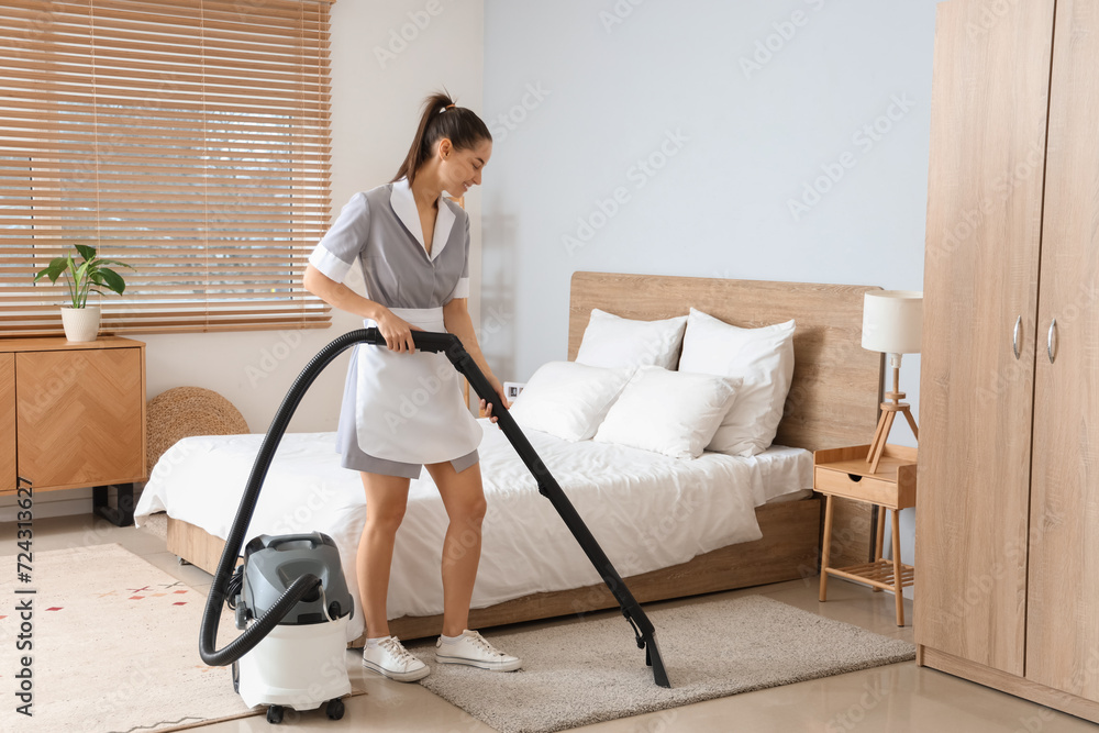 Young chambermaid cleaning carpet in bedroom