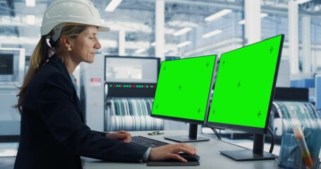 Caucasian Female Technician In Hardhat Working on Desktop Computer with Green Screen Chromakey Mock-Up Display in Electronics Factory Office. Autonomous Technological Research and Development Facility