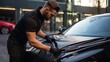 Car detailing concept: man cleaning black car with microfiber cloth, selective focus on shiny surface