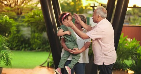 Wall Mural - Indian Asian happy aged old elder male man woman young female lady standing hold cute child baby girl kid play outdoor home park older lover couple family funny talk enjoy fun joy outside house garden