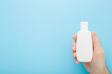 Wall Mural - Young adult man hand holding white plastic cream bottle on blue table background. Pastel color. Care about clean and soft body skin. Male beauty product. Closeup. Top down view. Empty place for text.