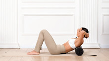 Young athletic female trainer doing fascia exercises on the floor - Caucasian woman using a foam roller - a tool to relieve back tension and relieve muscle pain.