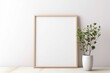 White light frame mockup with green plant in a pot on a floor. Frame with copy space. Minimalistic interior design with empty frame and plant