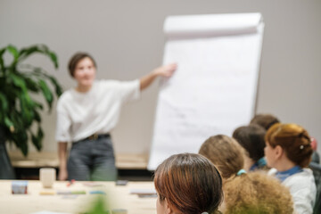 Rear view of engaged audience listening to a female speaker during a professional workshop or business training session.