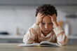 © Prostock-studio - Stressed Little Black Boy Reading Book At Home And Touching Head