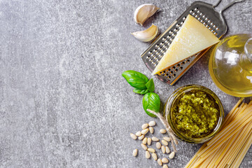 Wall Mural - Homemade pesto sauce in small jar and ingredients for pasta on gray concrete background with copy space. Traditional Italian cuisine, recipe, restaurant menu, banner, header