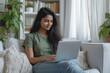 Young Indian woman wearing jeans and green t-shirt sitting working in laptop in white home office