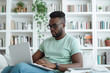 © wolfhound911 - Young African American man wearing jeans and green t-shirt sitting working in laptop in stylish white home office