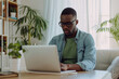© wolfhound911 - Young African American man wearing jeans and green t-shirt sitting working in laptop in stylish white home office