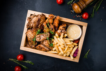 Poster - Fried chicken fillet and legs with french fries, onions, tomatoes, sauce and greens in wooden box.