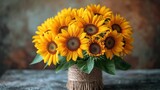 Fototapeta  -  a vase filled with lots of yellow sunflowers on top of a wooden table next to a brown and white wall and a rope wrapped vase filled with a bunch of yellow sunflowers.