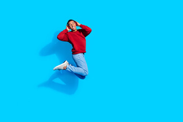 Poster - Photo of joyful positive man wear red trendy sweatshirt listen music wireless headphones empty space isolated on blue color background