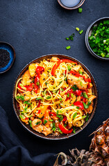 Stir fryed egg noodles with chicken, pineapple, paprika, green onion, soy sauce and sesame seeds in bowl. Asian cuisine dish. Black table background, top view