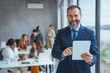 © Dragana Gordic - Shot of a successful senior businessman standing in office with digital tablet. Elegant business multitasking multimedia man using devices at office.