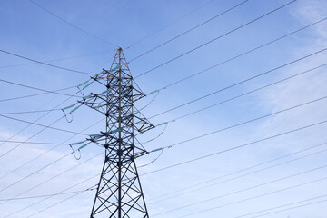 A high-voltage mast with wires on a background of blue sky with light clouds. Bottom view.