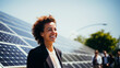 © GT77 - Cheerful young woman with curly hair and bright smile, in business suit, on background with solar panels at sunny day, renewable energy, sustainability and business innovation concept