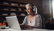 © Maria - A woman in her 60s wearing a headset is working on a laptop