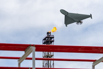 Wall Mural - A military drone flies over an oil refinery, fire burning.