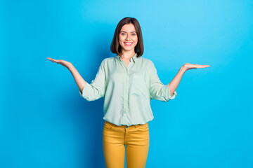 Poster - Portrait of pleasant nice girl with stylish hair wear teal shirt palms comparing products empty space isolated on blue color background