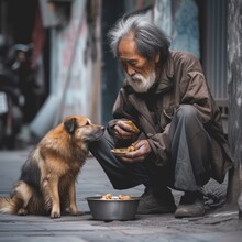 A Man Dressed In Casual Clothing Kneels On The Ground Of A Busy Street, Tenderly Feeding His Loyal Dog As They Enjoy An Outdoor Adventure Together