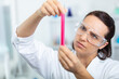young attractive concentrated female scientist in protective eyeglasses examines test-tube