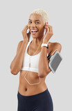 Fototapeta Koty - Fitness workout, happy smiling woman wears earphones of mobile phone on arm band, african latin american female athlete in sportswear, exercising in gym or jogging, isolated on grey background