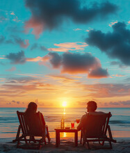 Happy Couple On Beach Chairs With A Side Table With Cocktails Enjoy Luxurious Sunset On The Beach During Summer Vacations.