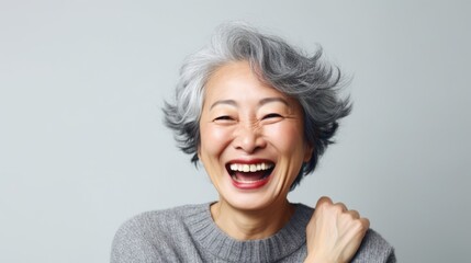 Wall Mural - An older woman wearing a grey sweater is captured in a moment of laughter. This image can be used to depict joy, happiness, and positive emotions.