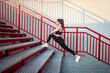 © khosrork - Full length portrait of slim athletic flexible woman wearing black sportswear doing physical exercising stretching legs before workout on stairs training her body outdoor.