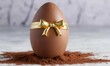 Milk chocolate in the shape of an egg with a golden bow in the background. Easter celebration concept.