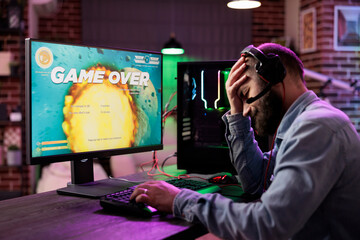 Canvas Print - Gamer feeling depressed after losing online multiplayer action videogame match, being outsmarted by rival players. Dejected man getting headache from frustration after seeing game over screen