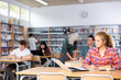 © JackF - European fifteen-year-old schoolgirl searches for information on a laptop and writes an notes in a copybook while doing homework in the school library