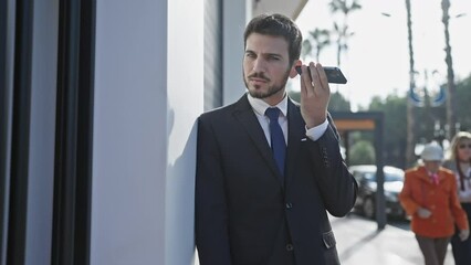 Wall Mural - Handsome bearded businessman using smartphone on a sunny urban street.