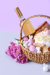 Wall Mural - Basket with Easter eggs, cake, bottle of wine and tulip flowers on lilac background