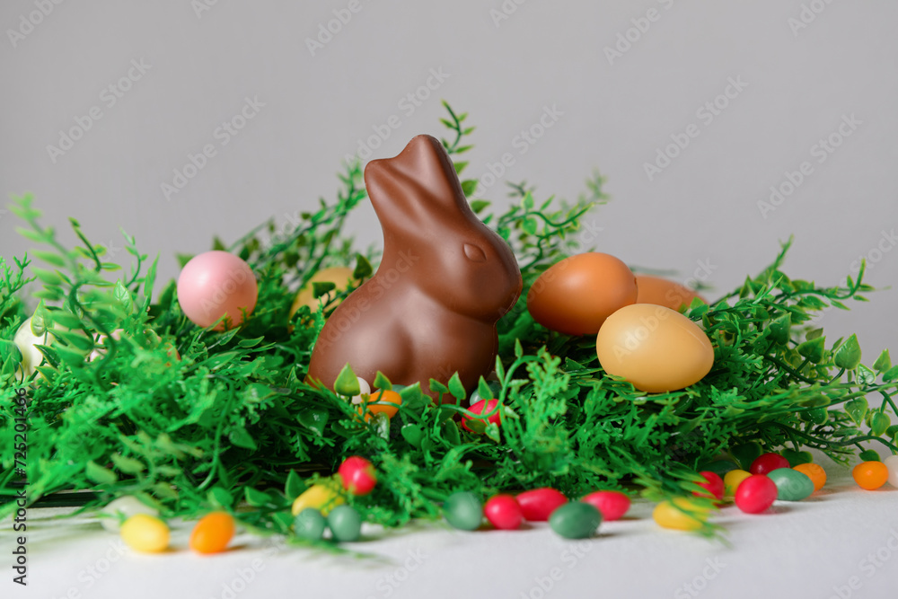 Chocolate bunny, Easter eggs and candies in plant leaves on white table