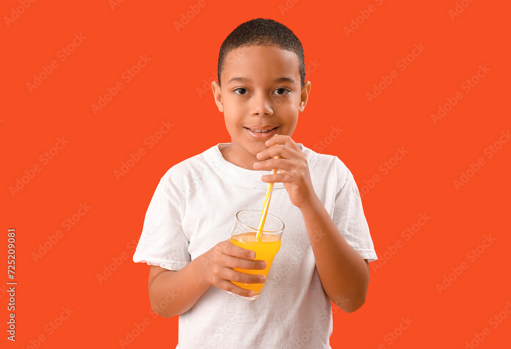 Little African-American boy drinking orange juice on red background