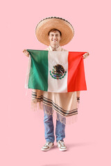 Poster - Young man in sombrero and poncho holding Mexican flag on pink background