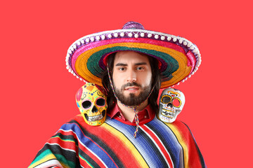 Canvas Print - Handsome young Mexican man with painted skulls on red background. Celebration of Day of the Dead