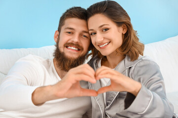 Canvas Print - Happy couple in love making heart gesture in bedroom